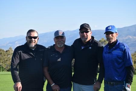 Four men standing next to each other on a golf course.